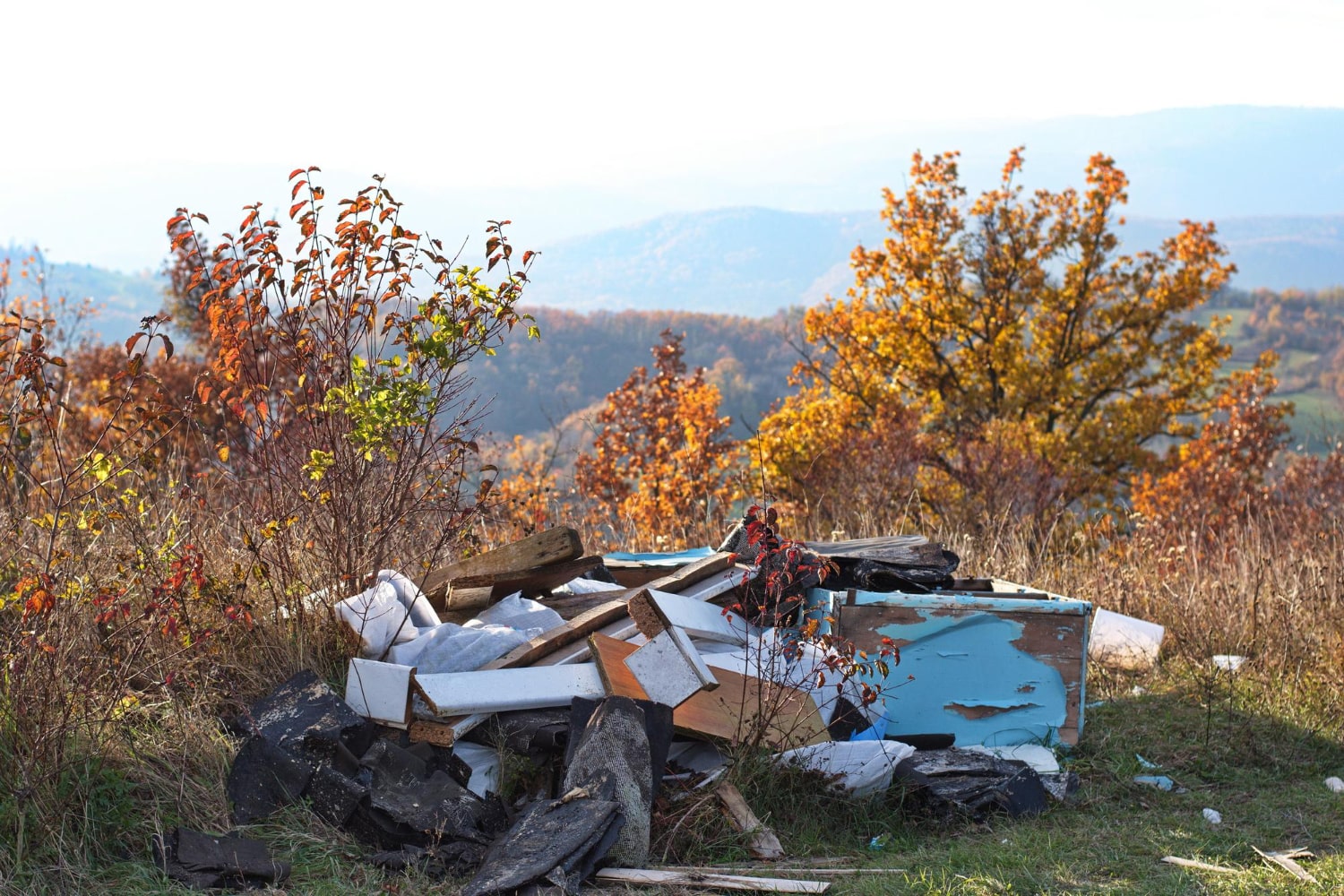 A pile of discarded debris and garbage cluttered amidst colorful autumn foliage on a hillside.